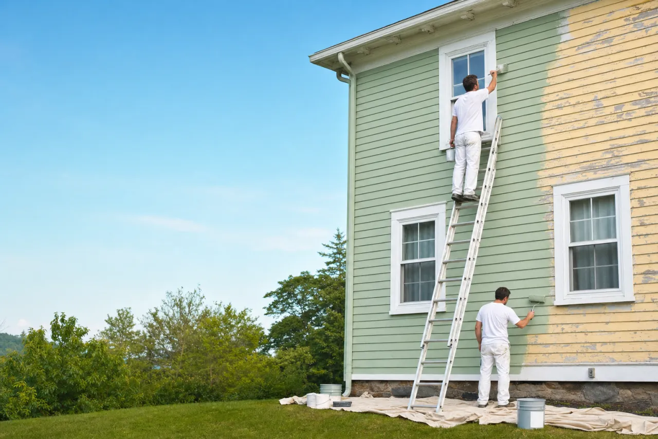 A paint crew repainting the siding of a two-story house
